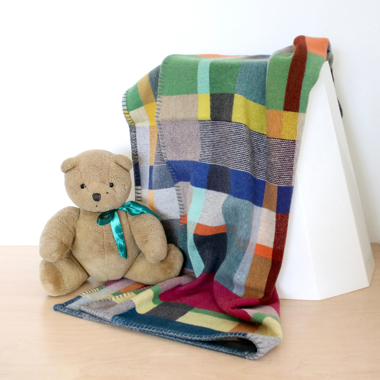 Colourful wool blanket draped over a white surface with a teddy bear sitting on it.