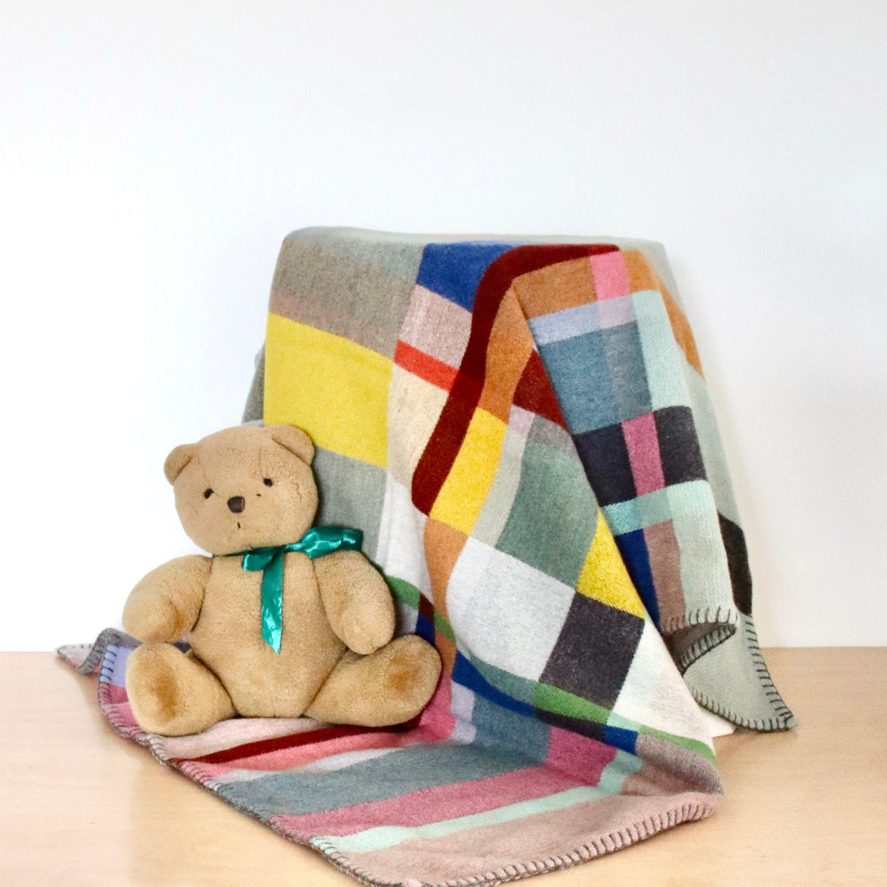 Colorful checkered blanket draped over a surface with a teddy bear sitting on it.