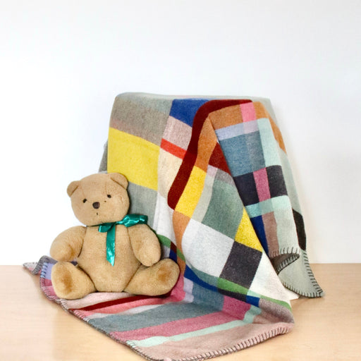 Colorful checkered blanket draped over a surface with a teddy bear sitting on it.