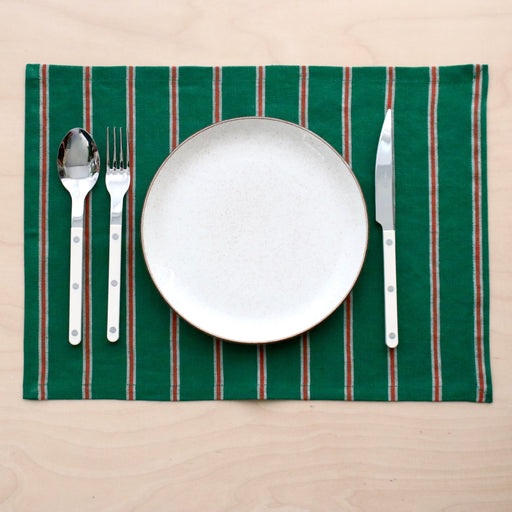 Placemat with green and red stripes, white plate, silverware on a beige background