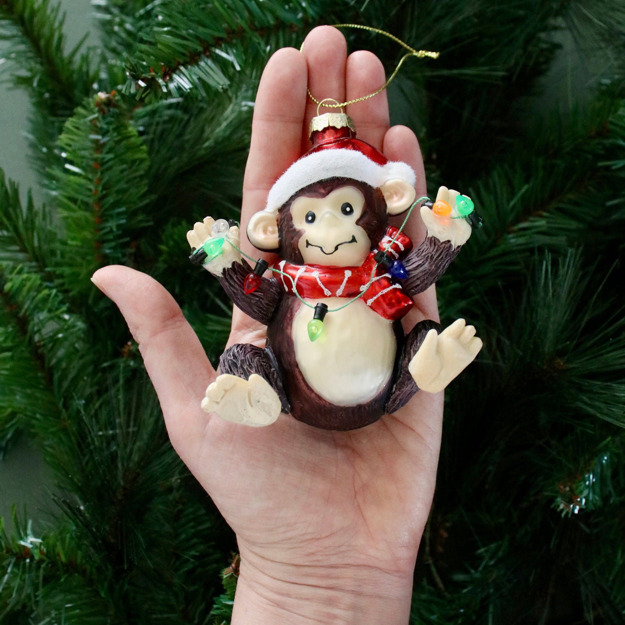 Monkey ornament with a Santa hat held in front of a Christmas tree.