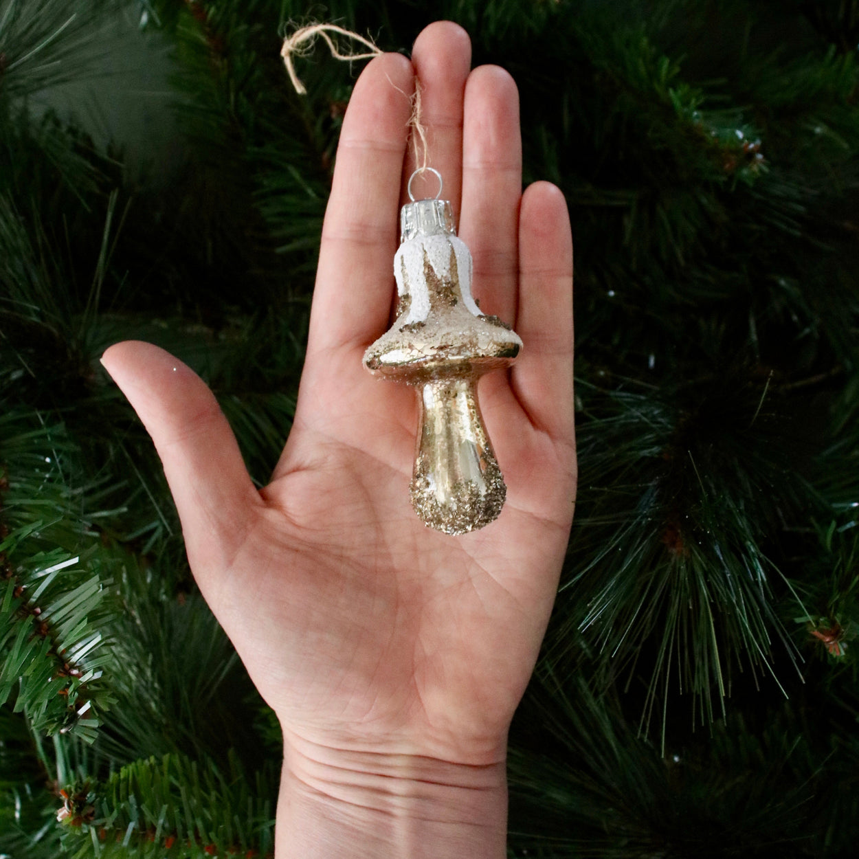 Hand holding a gold glass ornament against a green Christmas tree background