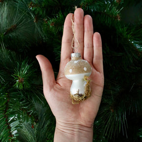 Hand holding a decorative mushroom ornament against a green pine tree background