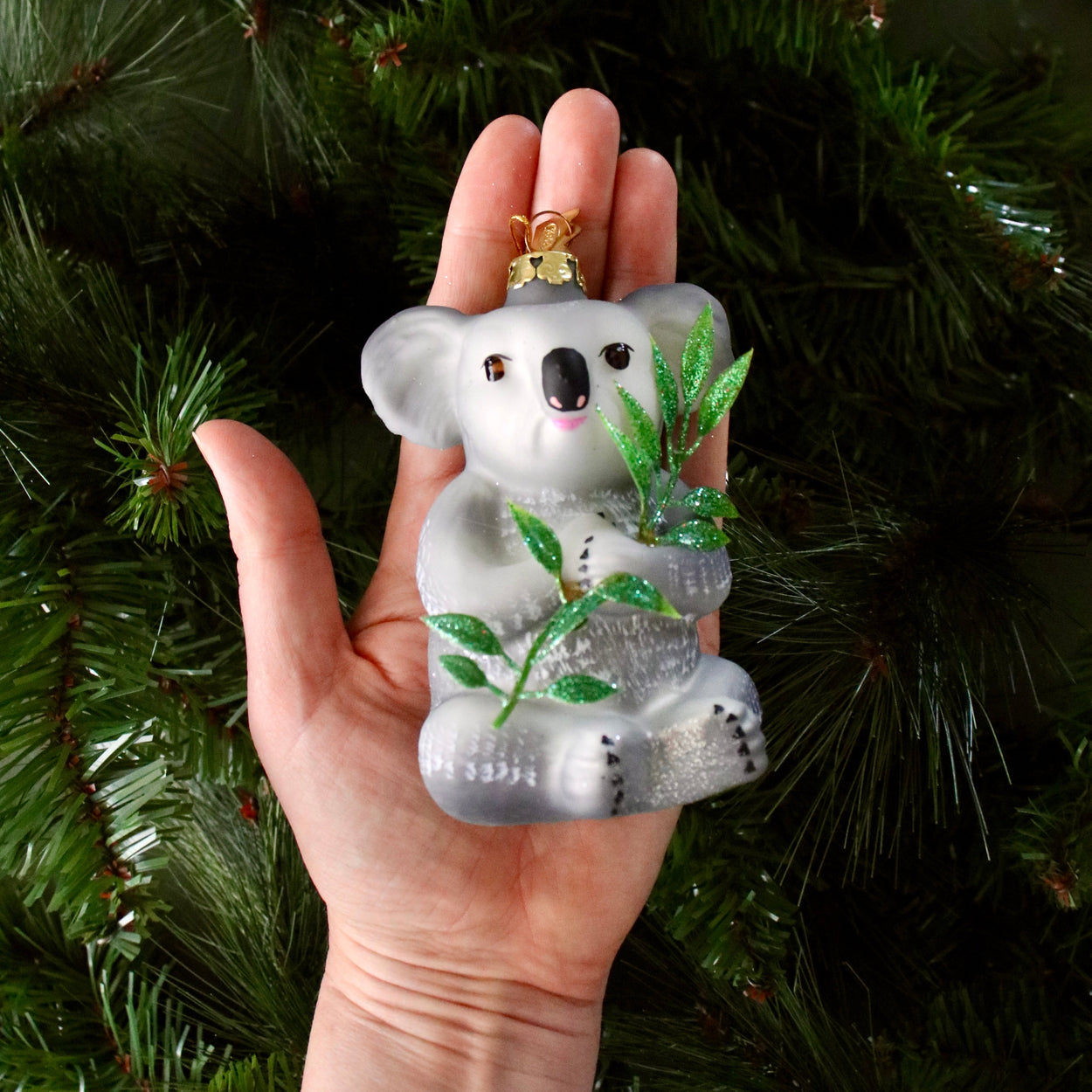 Glass koala ornament held in front of a Christmas tree