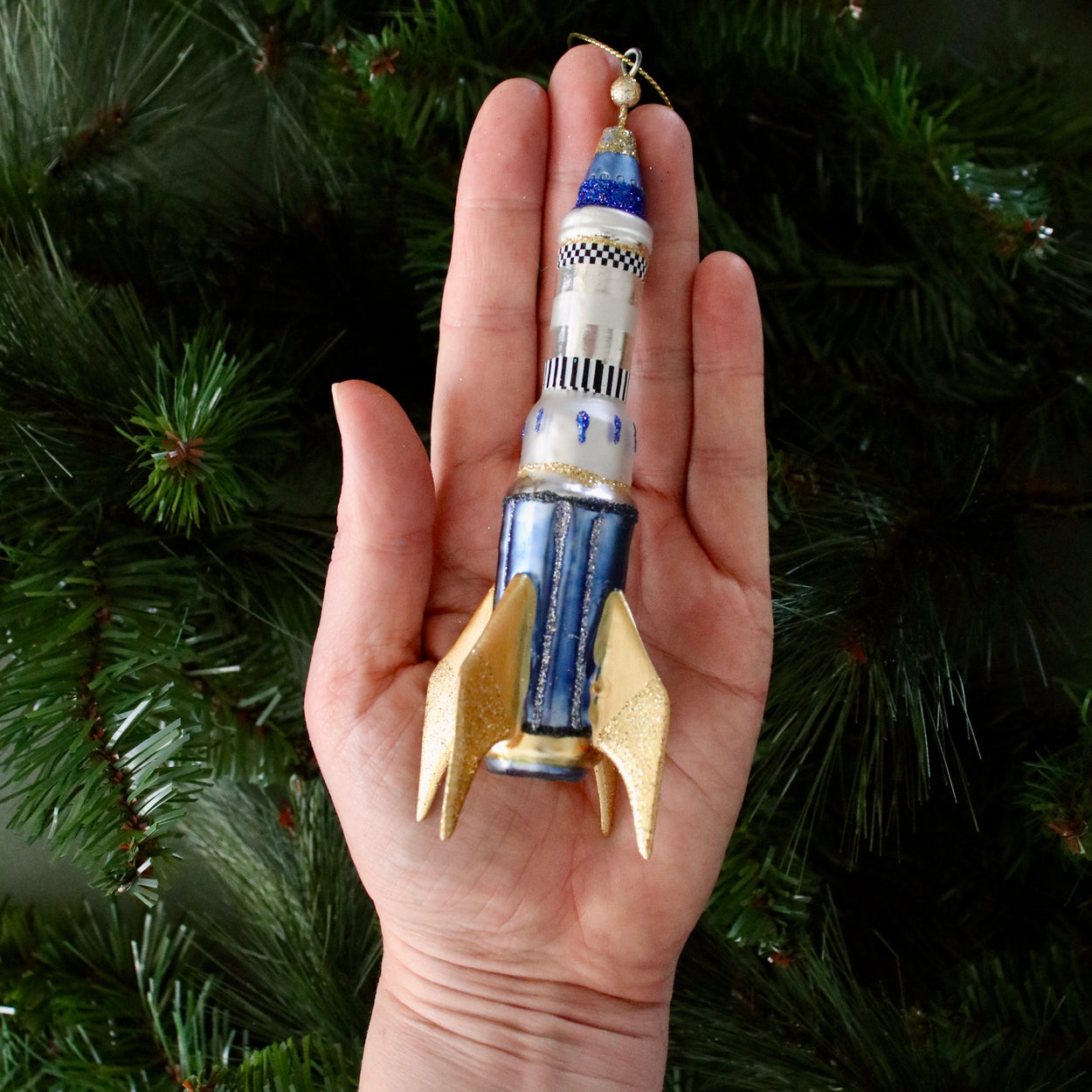 Rocket-shaped ornament held in a hand with a Christmas tree background