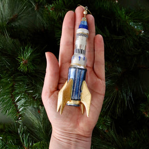 Rocket-shaped ornament held in a hand with a Christmas tree background