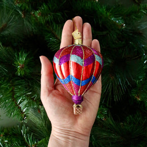 Hand holding a colorful hot air balloon ornament against a Christmas tree background