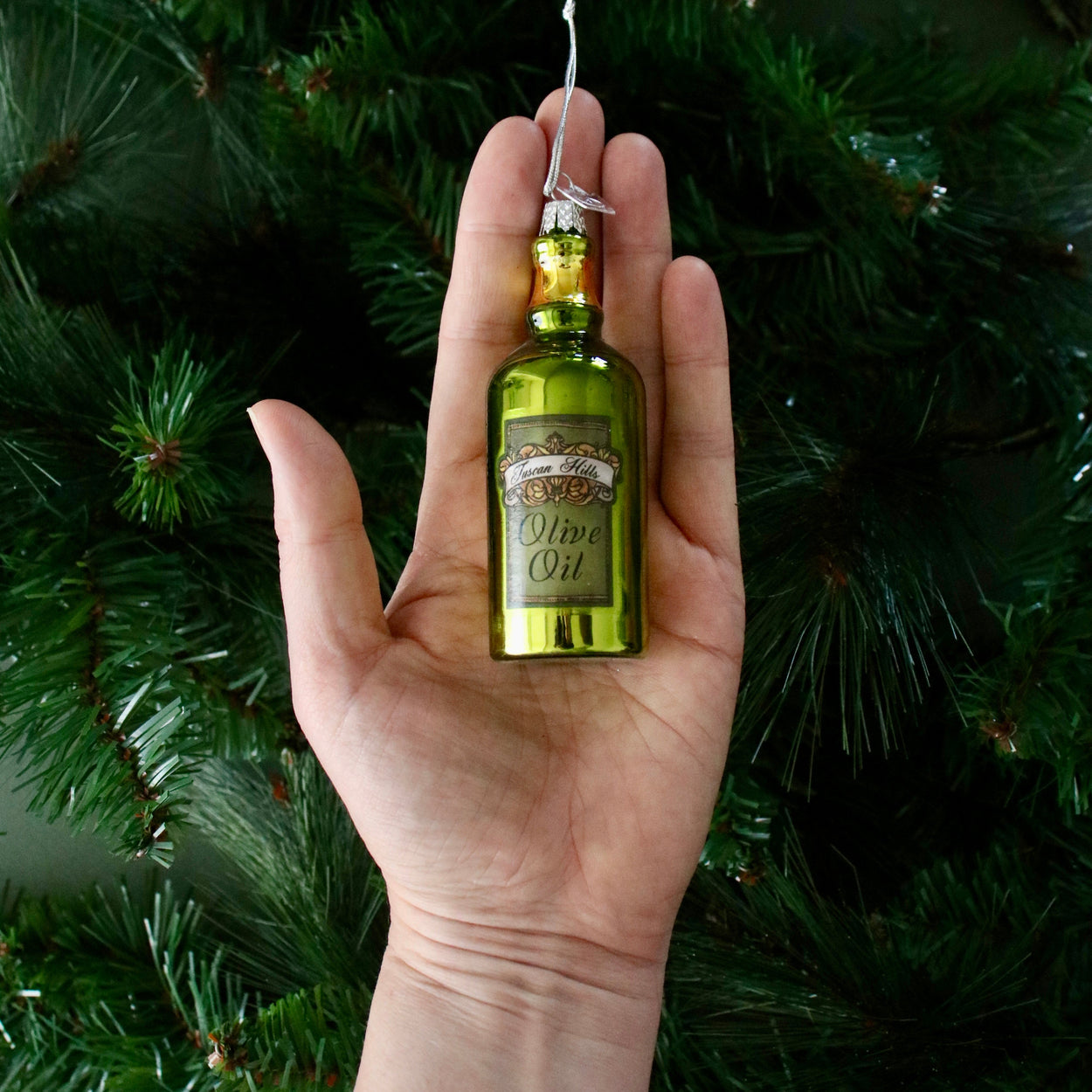 Hand holding a miniature olive oil bottle ornament against a green background