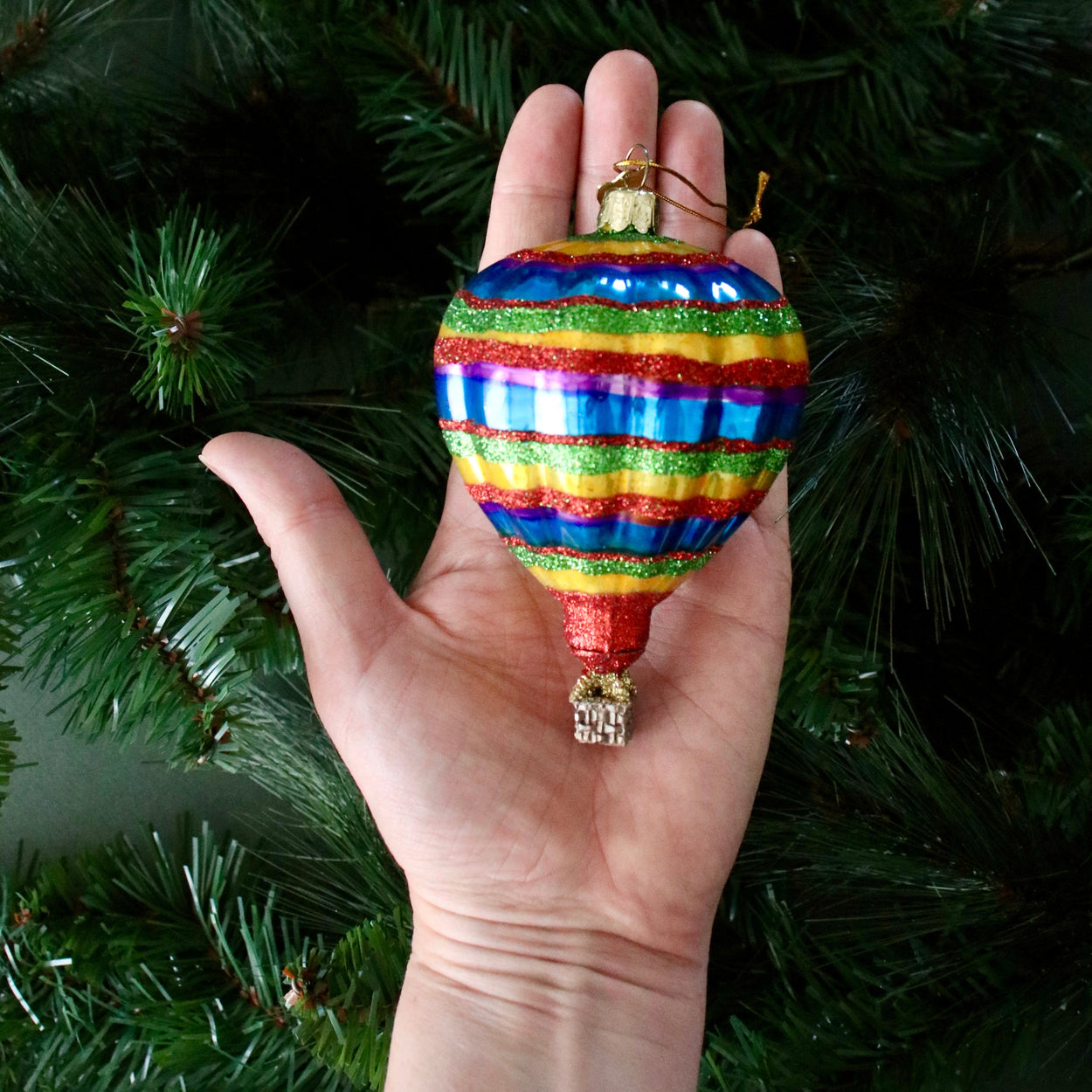 Hand holding a multicolored striped Christmas ornament against a green tree background