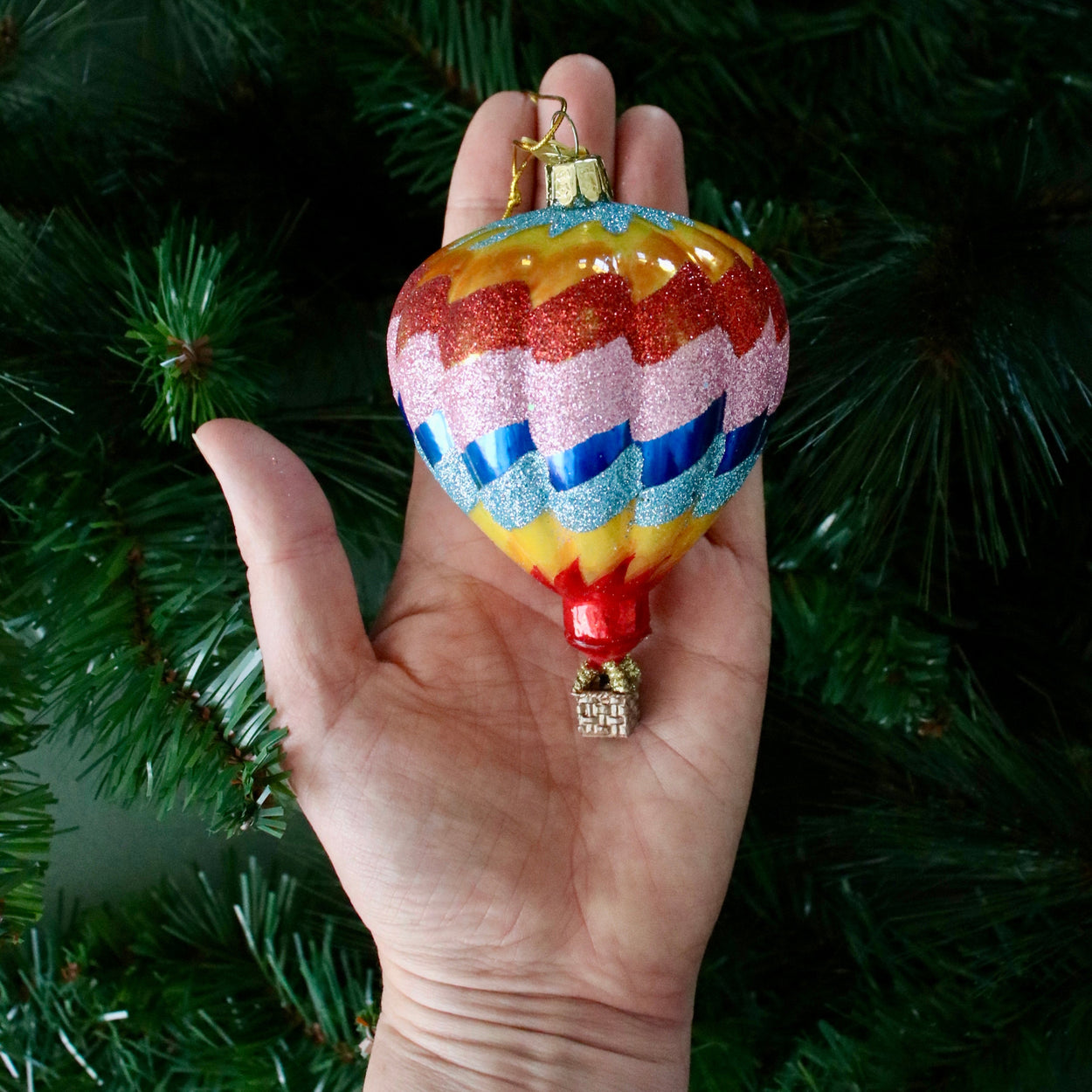 Colorful hot air balloon ornament held in front of a Christmas tree.