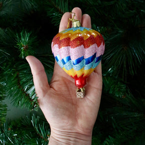 Colorful hot air balloon ornament held in front of a Christmas tree.