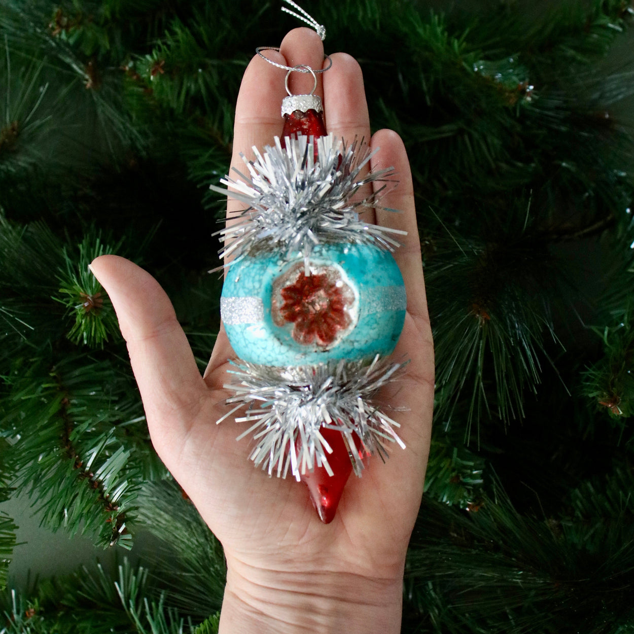 Hand holding a decorative ornament with a Christmas tree in the background