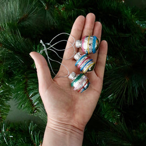 Hand holding three colorful glass Christmas ornaments against a green tree background