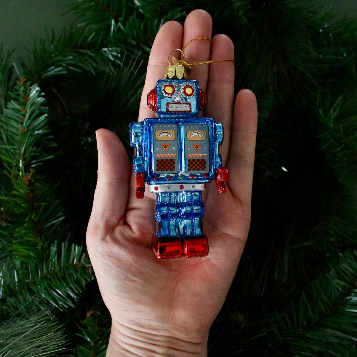 Hand holding a robot-shaped Christmas ornament against a green leafy background