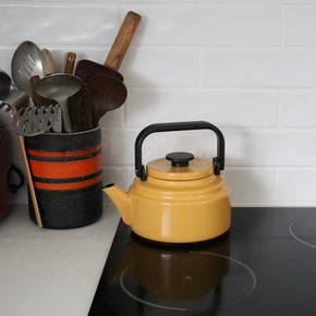 Yellow kettle on a stove with kitchen utensils in the background
