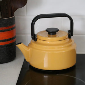 Yellow kettle with black handle on a stove, next to a black and red striped container.