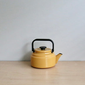 Yellow teapot with a black handle on a wooden surface and light gray background
