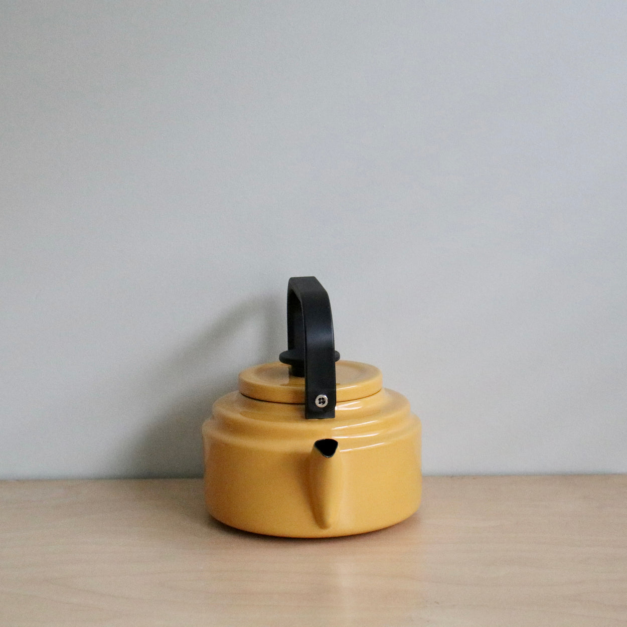 Yellow kettle with a black handle on a wooden surface and light gray background