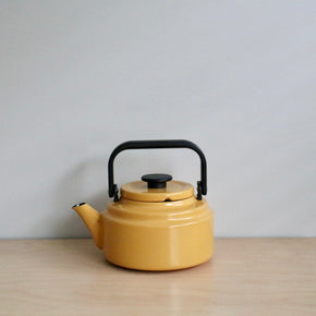 Yellow teapot with black handle on a light wooden surface and gray background