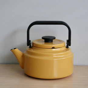 Yellow teapot with a black handle on a wooden surface and gray background
