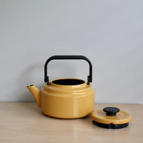 Yellow teapot with black handle and lid on a wooden surface