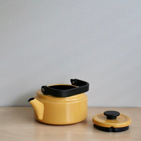 Yellow teapot with black handle and lid on a wooden surface