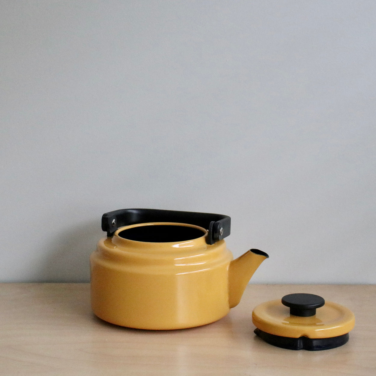 Yellow teapot with black handle and lid on a wooden surface against a gray background