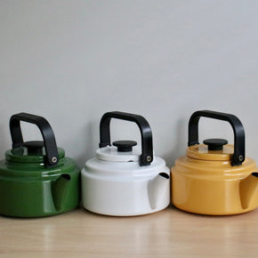 Three colorful kettles (green, white, yellow) with black handles on a wooden surface.
