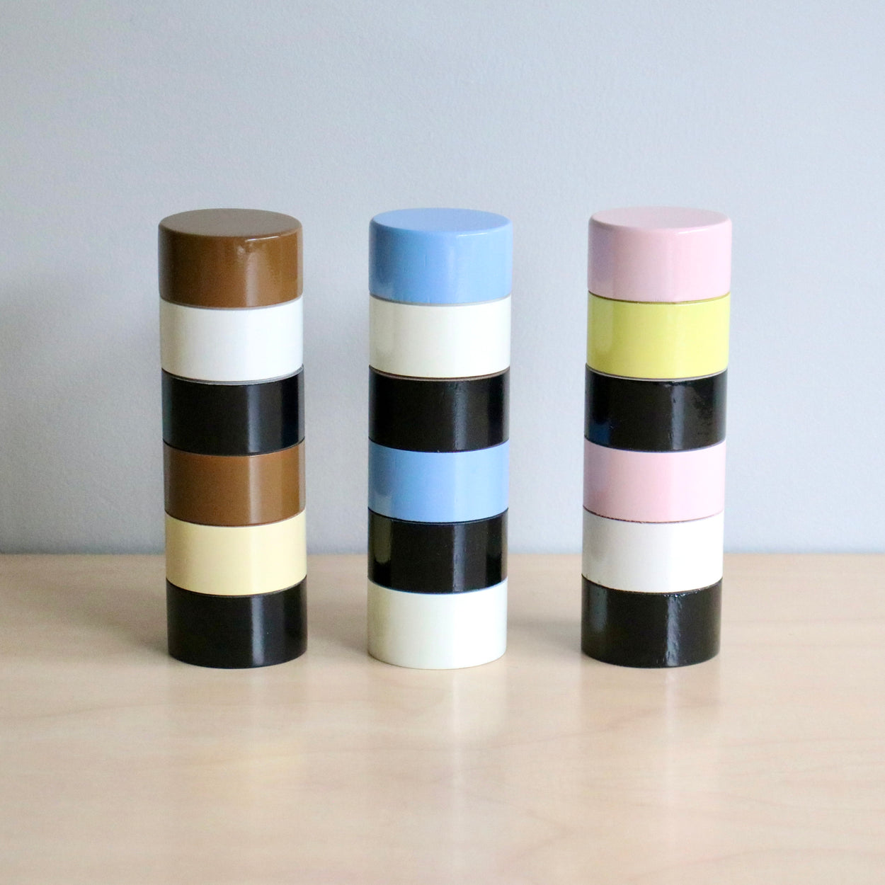 Three cylindrical pepper grinders with striped patterns on a wooden surface and light gray background
