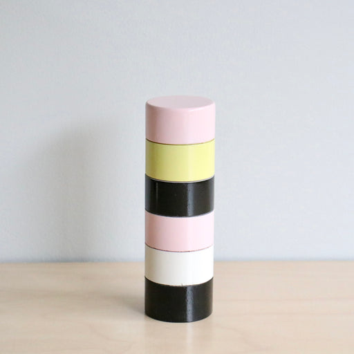 A cylindrical pepper grinder with colorful stripes on a light surface and white background