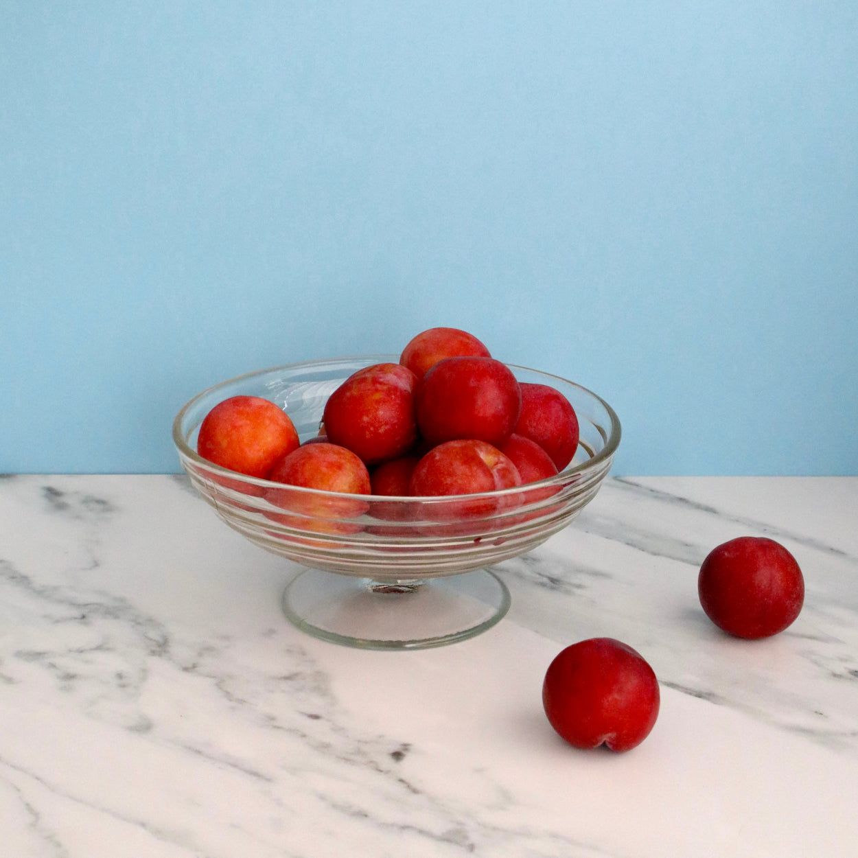 Glass bowl filled with red fruits on a marble surface with a light blue background