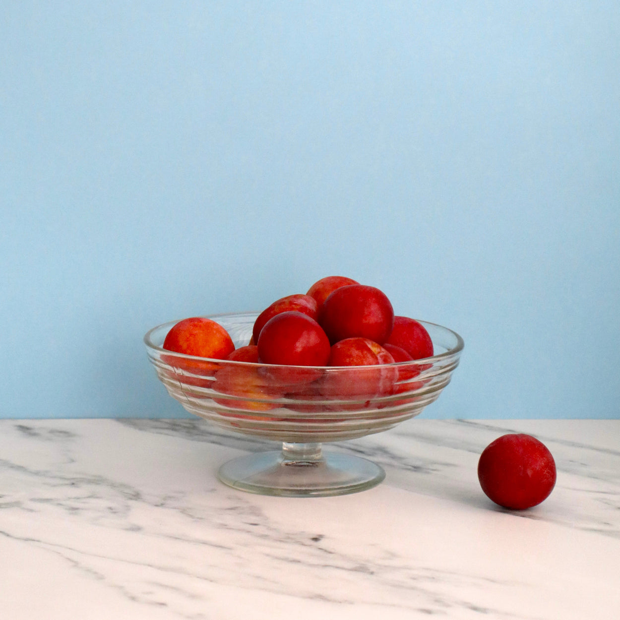 Glass bowl with red fruits on a marble surface against a light blue background