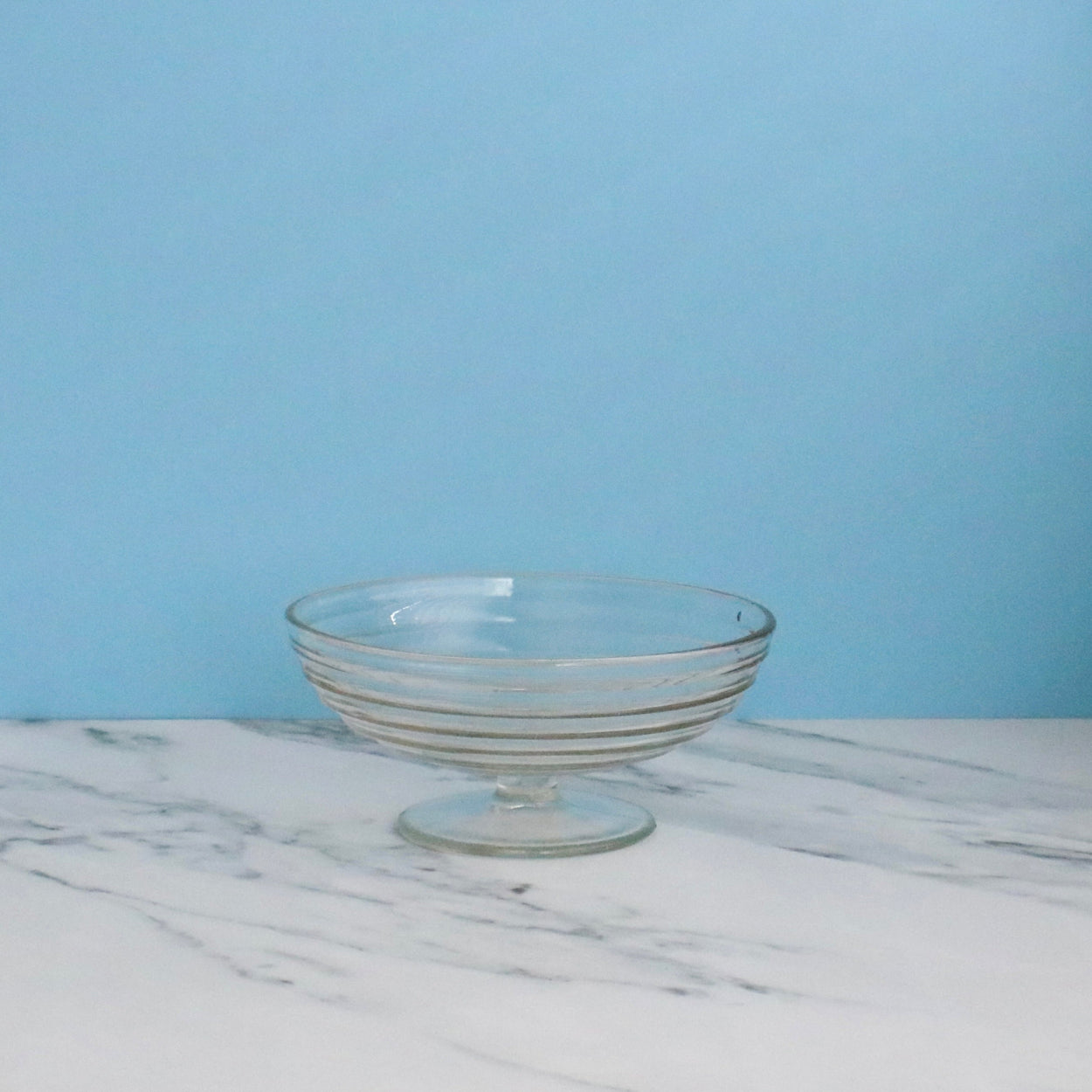 Clear glass bowl on a marble surface with a light blue background