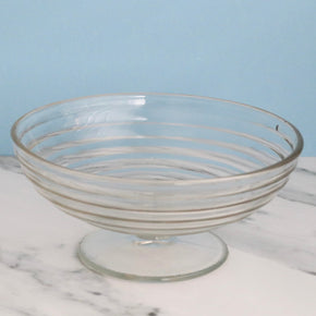Clear glass footed bowl on a marble surface with a light blue background