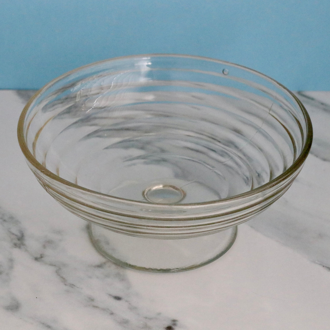 Clear glass bowl on a marble surface with a blue background