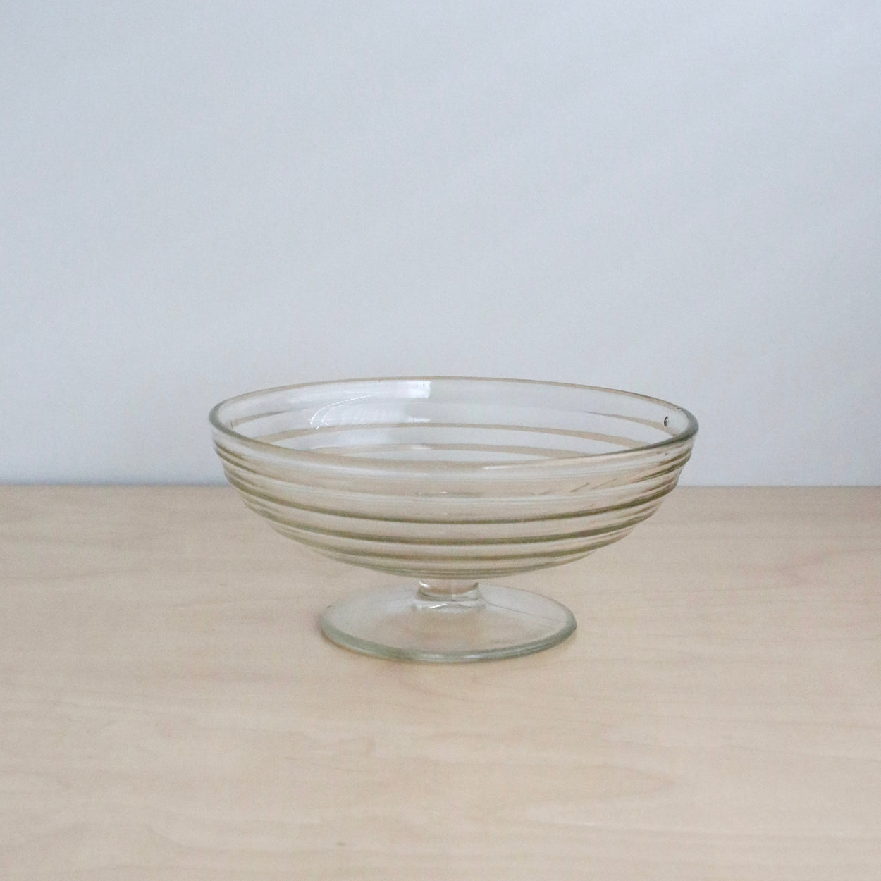 Clear glass footed bowl on a beige surface with a light gray background