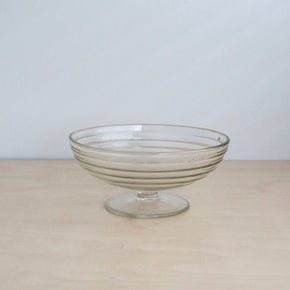 Clear glass footed bowl on a beige surface with a light gray background