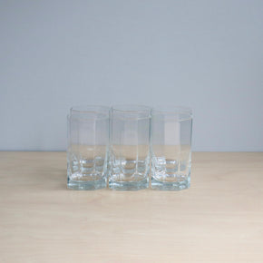 Three clear glass tumblers on a light surface with a light gray background