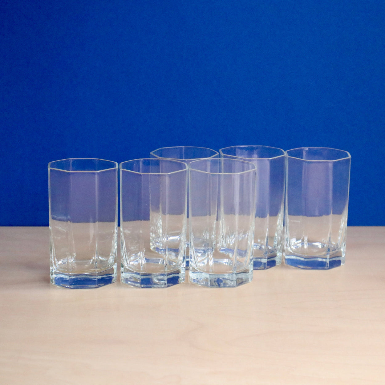 Set of six clear glasses on a beige surface with a blue background