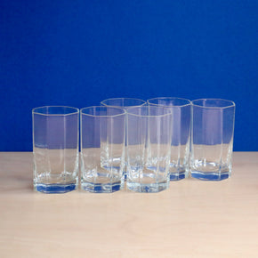 Set of six clear glasses on a beige surface with a blue background
