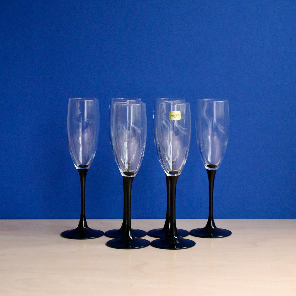 Six champagne flutes with black stems on a blue background