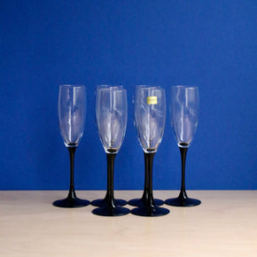 Six champagne flutes with black stems on a blue background