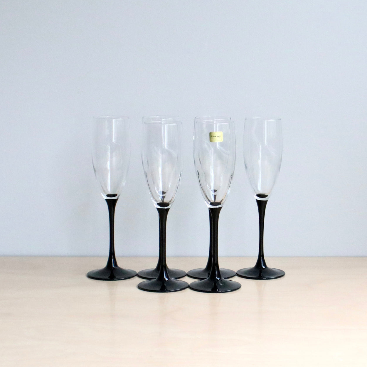 Six champagne flutes with black stems on a light surface and light gray background