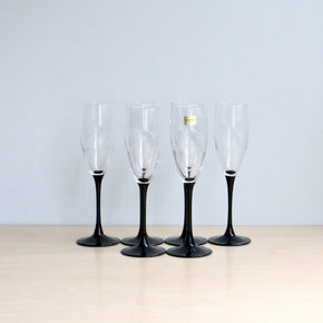 Six champagne flutes with black stems on a light surface and light gray background
