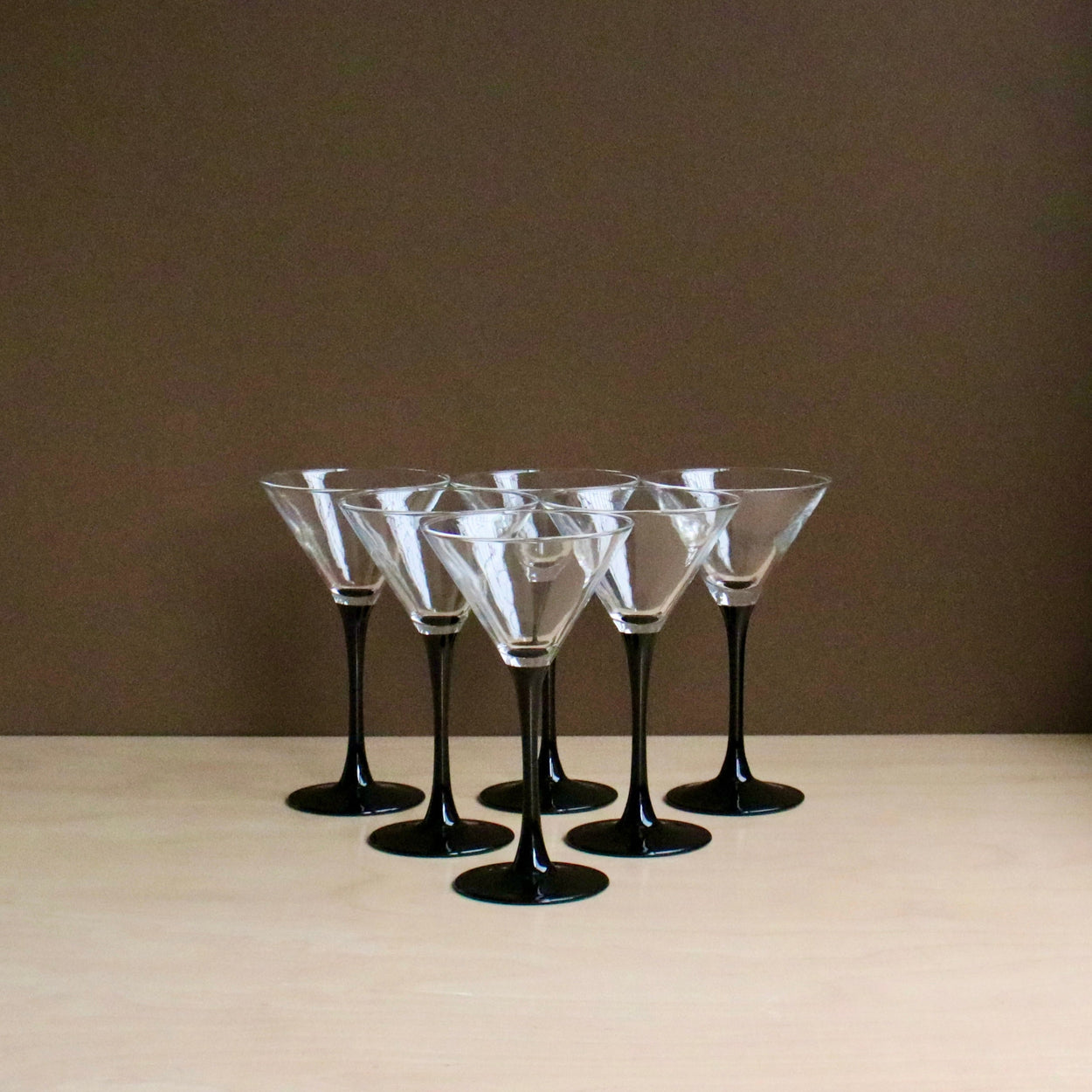 Set of six black-stemmed martini glasses on a beige surface with a brown background