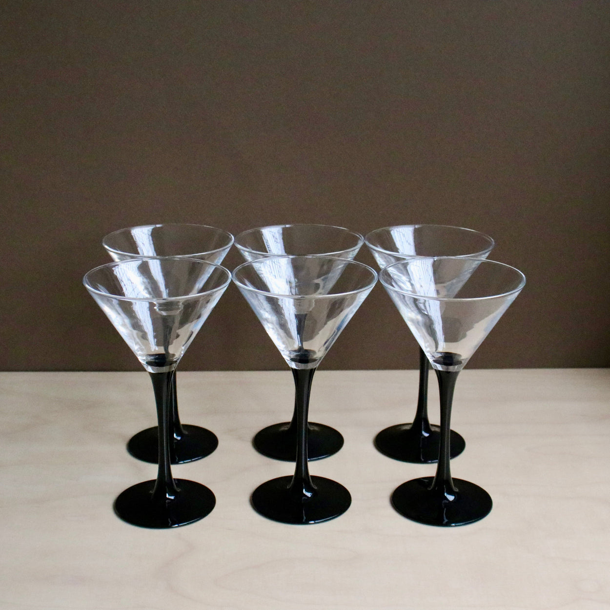 Set of six clear martini glasses with black stems on a beige surface.
