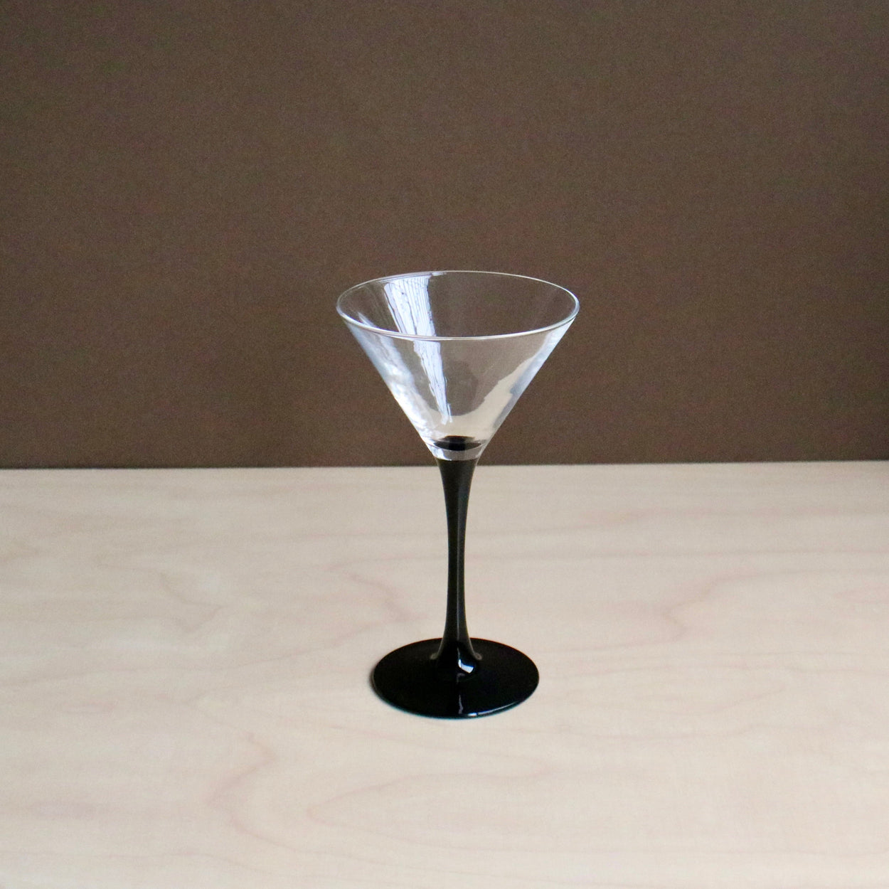 Clear martini glass with black base on a beige surface and brown background