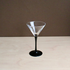 Clear martini glass with black base on a beige surface and brown background