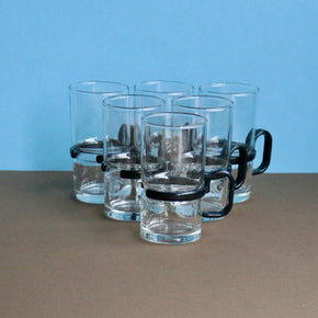 Set of clear glass mugs with black handles on a brown surface with a blue background