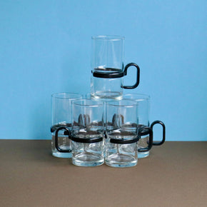 Set of clear glass mugs with black handles on a brown surface with a blue background